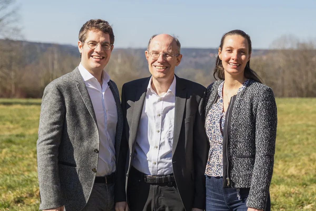 Three people stand side by side outdoors, smiling at the camera.