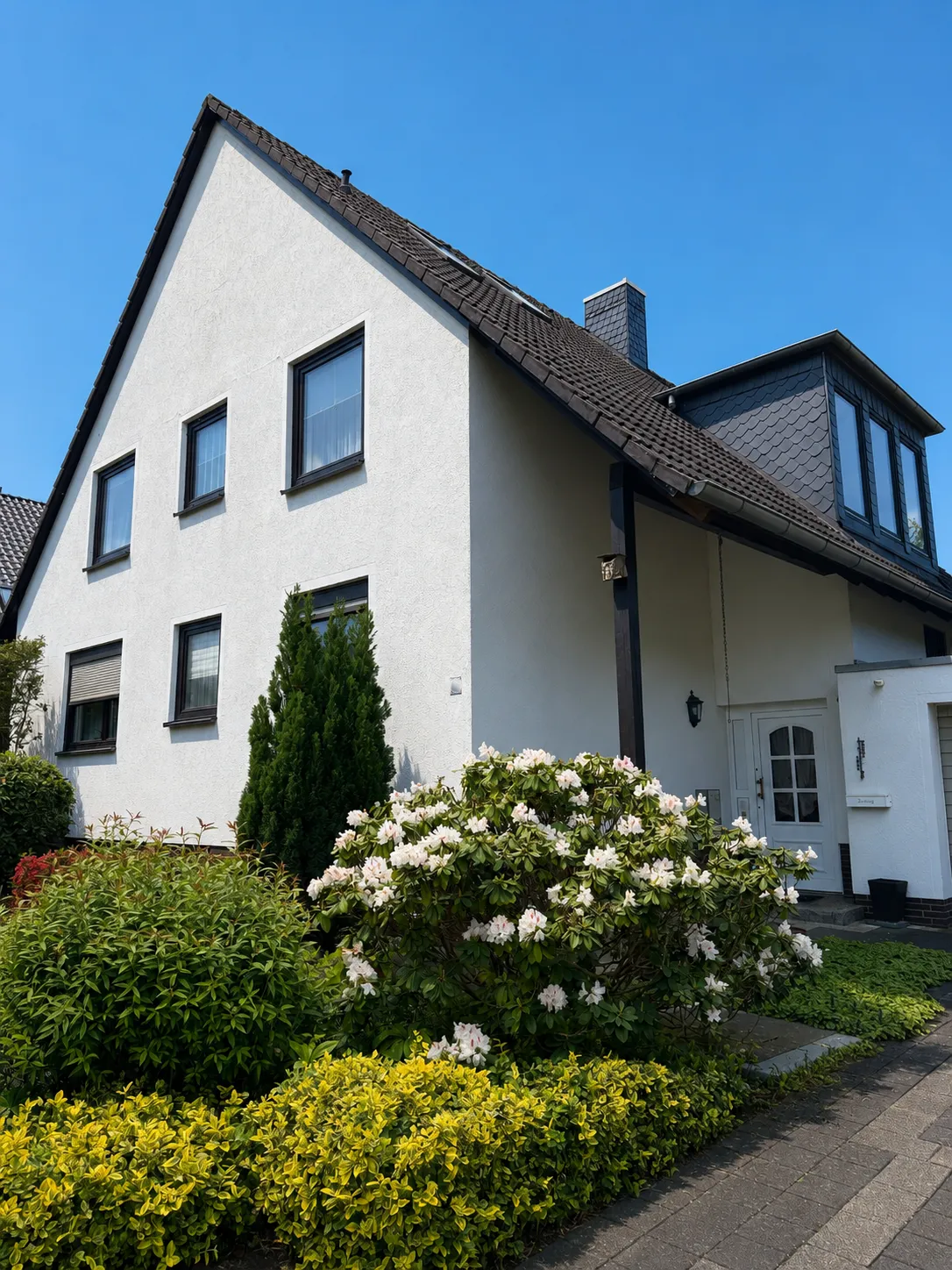 Ein weißes Haus mit dunklem Dach und gepflegtem Vorgarten.