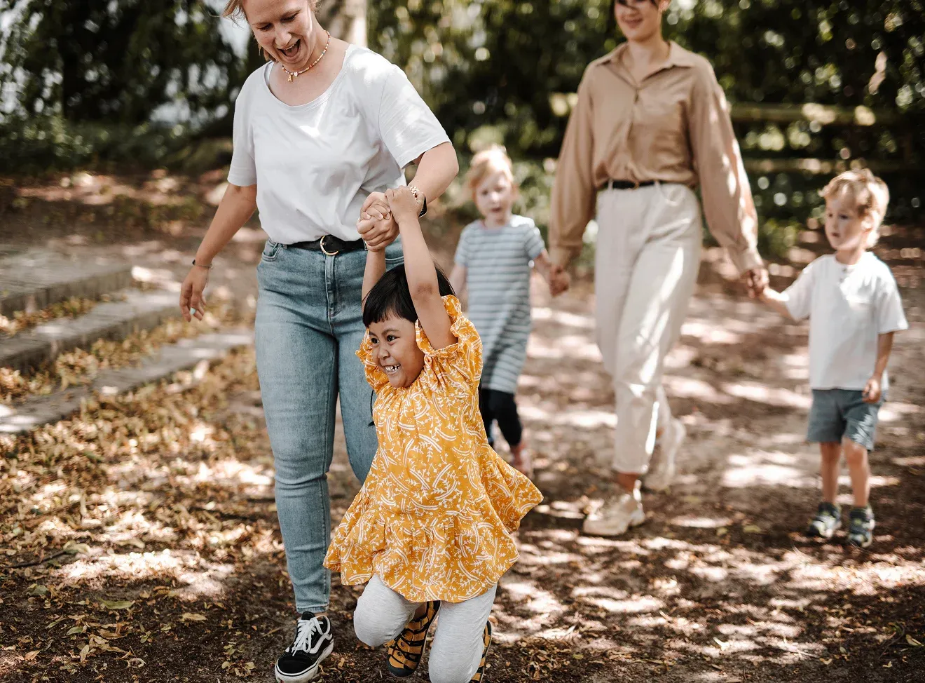 Zwei Frauen und drei Kinder spazieren lachend auf einem Weg im Freien.