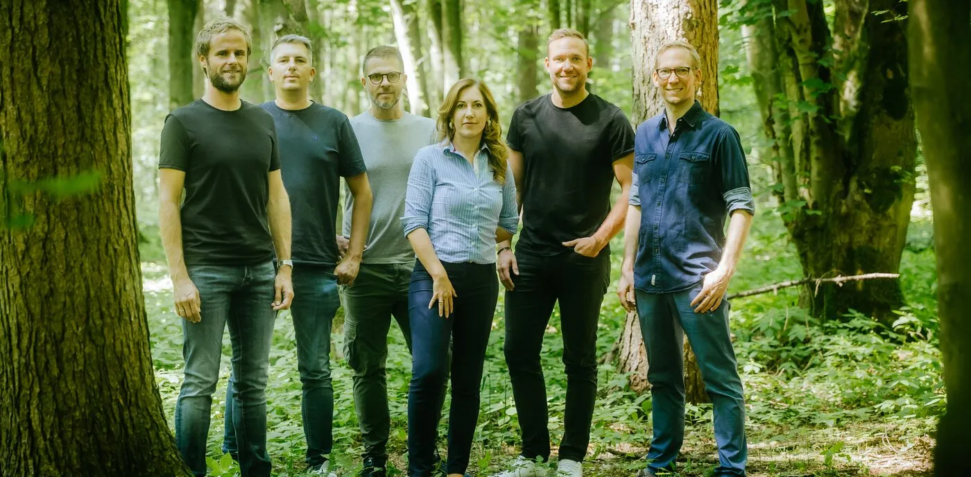 Sechs Teammitglieder stehen in einem Wald.