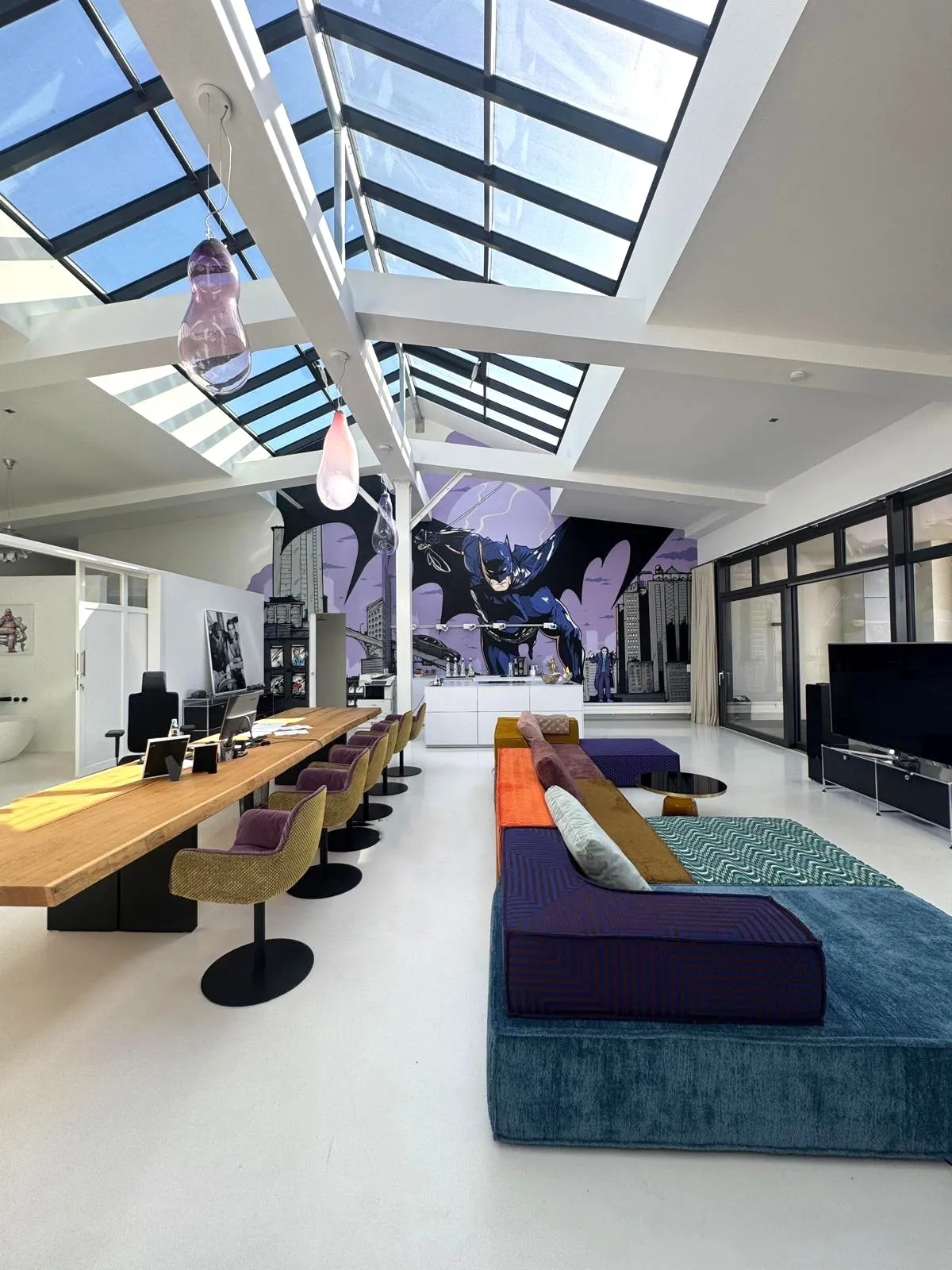 Ein großes, offenes Büro mit einem langen Tisch, bunten Sofas und einem Oberlichtdach.