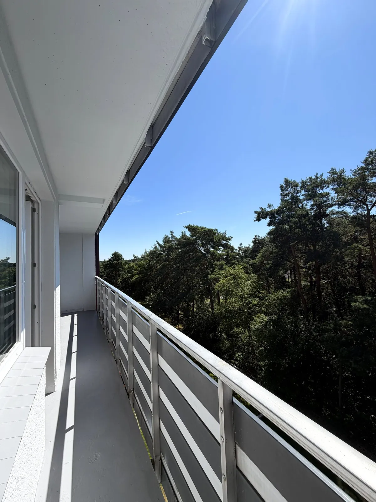 Ein langer Balkon mit Blick auf einen Wald unter blauem Himmel.